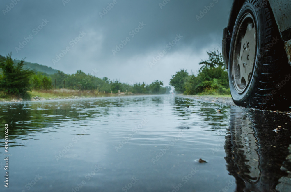 Detail of the rear wheel of a car driving in the rain on a wet road ...
