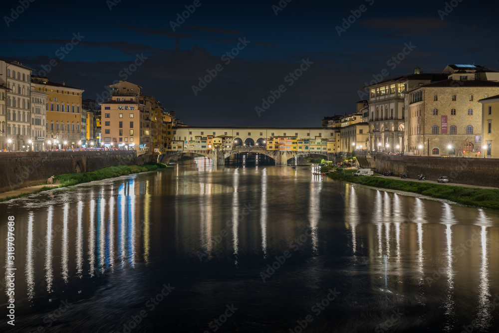 Ponte Vecchio in historical center downtown in Florence during sunrise with water reflections in Arno river
