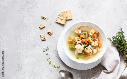 Vegetable soup with egg pancakes on light grey background. Traditional German Flaedlesuppe and Austrian Frittatensuppe.  photo