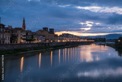 Florence old historical buildings reflecting in Arno river during a overcast sunrise morning with warm sun light