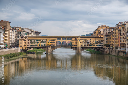Ponte Vecchio in historical center downtown in Florence during sunrise with water reflections in Arno river © Michele