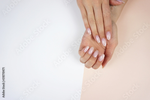 Classic pink manicure. Young woman's hands on peach and white background.