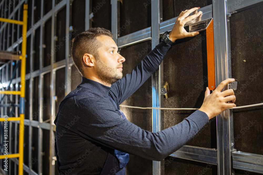 Make soundproofing in room. Man installs metal profiles on the wall. Carpenter measure the level of wall. Horizontal. Renovation at home. Building construction indoor. .. Make soundproofing in room. Man installs metal profiles on the wall. Carpenter measure the level of wall. Horizontal. Renovation at home. Building construction indoor. ..