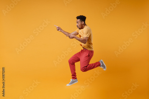 Side view of young african american guy in casual clothes posing isolated on yellow orange background studio portrait. People lifestyle concept. Mock up copy space. Jumping point index fingers aside.