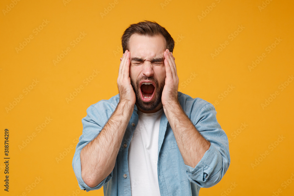 Young bearded man in casual blue shirt posing isolated on yellow orange background studio portrait. People lifestyle concept. Mock up copy space. Screaming, putting hands on head, keeping eyes closed. Young bearded man in casual blue shirt posing isolated on yellow orange background studio portrait. People lifestyle concept. Mock up copy space. Screaming, putting hands on head, keeping eyes closed.