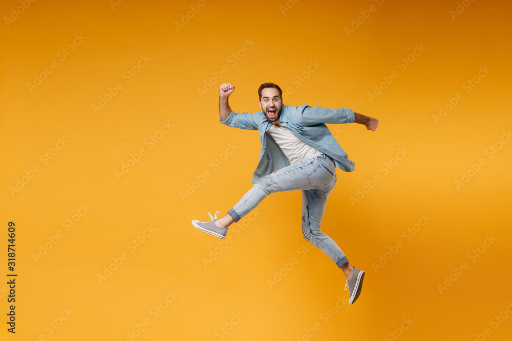 Side view of excited young bearded man in casual blue shirt posing isolated on yellow orange background studio portrait. People sincere emotions lifestyle concept. Mock up copy space. Jumping running.