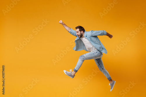Cheerful young bearded man in casual blue shirt posing isolated on yellow orange background studio portrait. People lifestyle concept. Mock up copy space. Jumping with outstretched hand like Superman. photo