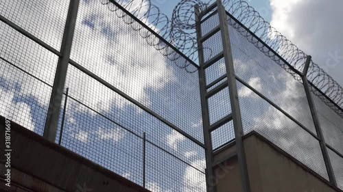 high prison fence with barbed wire against the blue sky. camera rises slowly up