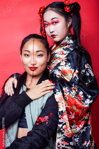 two pretty geisha girls friends: modern asian woman and traditional wearing kimono posing cheerful on red background