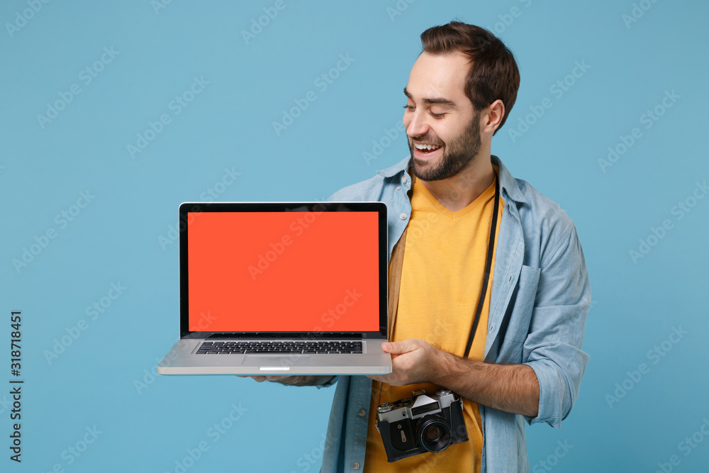 Smiling traveler tourist man in casual clothes with photo camera isolated on blue background. Passenger traveling abroad on weekends. Air flight journey. Holding laptop pc computer with blank screen.