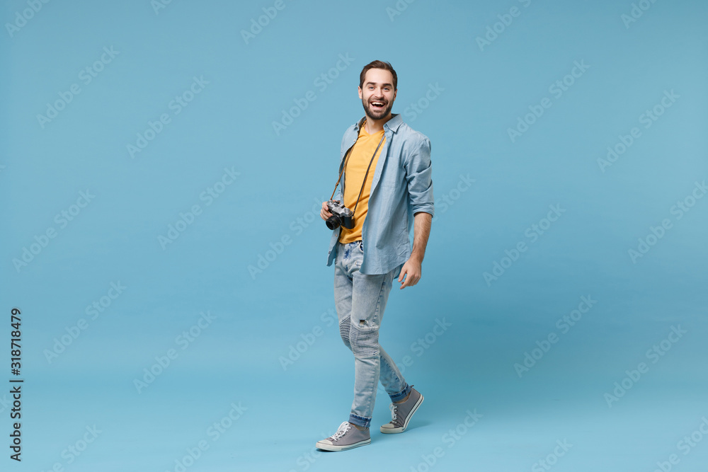 Laughing traveler tourist man in yellow summer casual clothes with photo camera on neck isolated on blue background. Male passenger traveling abroad on weekends getaway. Air flight journey concept. Laughing traveler tourist man in yellow summer casual clothes with photo camera on neck isolated on blue background. Male passenger traveling abroad on weekends getaway. Air flight journey concept.