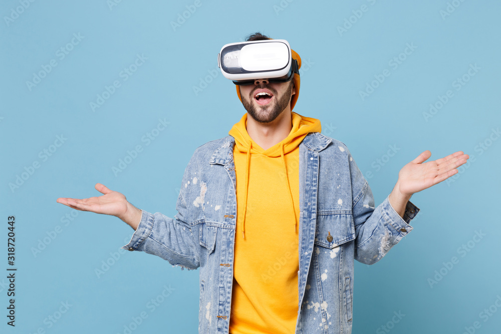 Young hipster guy in fashion jeans denim clothes posing isolated on pastel blue wall background studio portrait. People lifestyle concept. Mock up copy space. Watching in headset, spreading hands. Young hipster guy in fashion jeans denim clothes posing isolated on pastel blue wall background studio portrait. People lifestyle concept. Mock up copy space. Watching in headset, spreading hands.