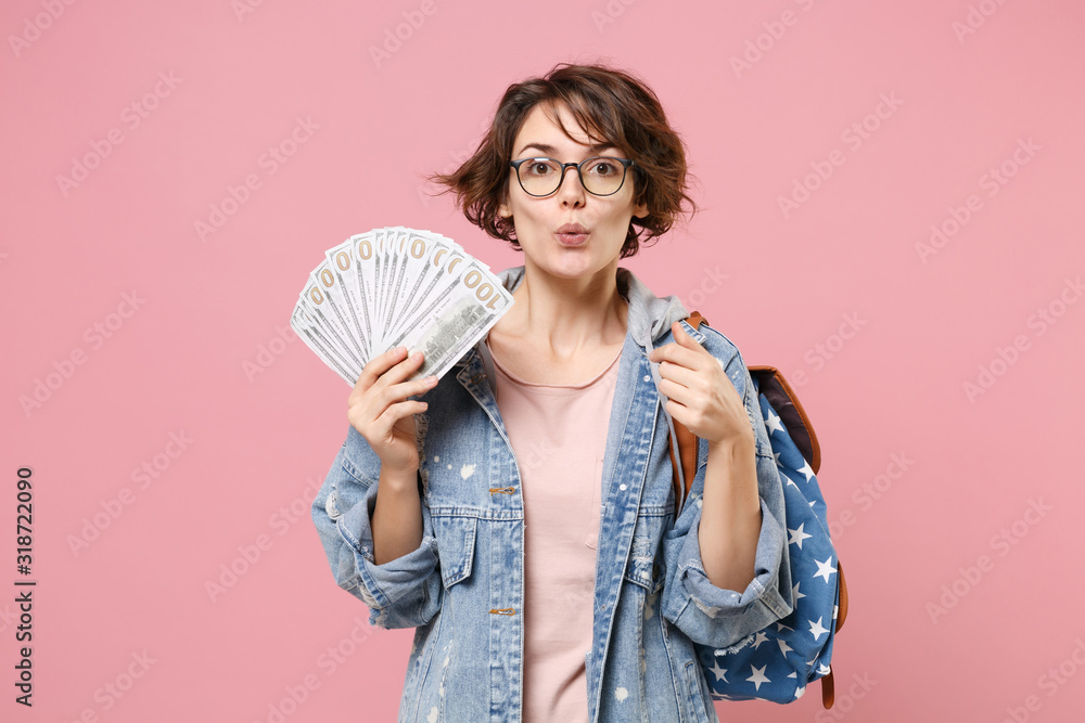Amazed girl student in denim clothes glasses backpack isolated on pastel pink background. Education in school university college concept. Pointing index finger on herself hold fan of dollar banknotes. Amazed girl student in denim clothes glasses backpack isolated on pastel pink background. Education in school university college concept. Pointing index finger on herself hold fan of dollar banknotes.