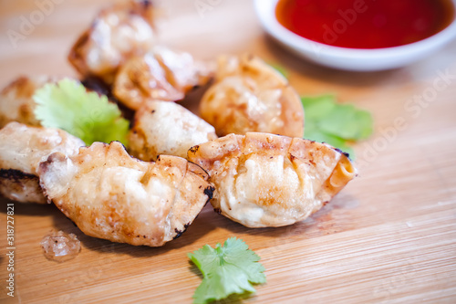 Crispy deep-fried wontons on wooden plate serve with sweet chilli sauce.