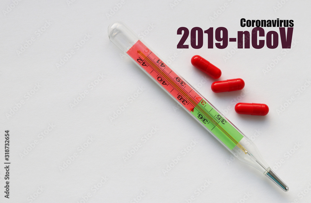 Three capsules and a thermometer on a light background and words in dark font: 2019-nCoV coronavirus. Selective focus. Copy space