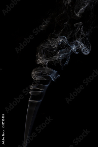 Delicate column of smoke from incense stick isolated on black background, selective focus