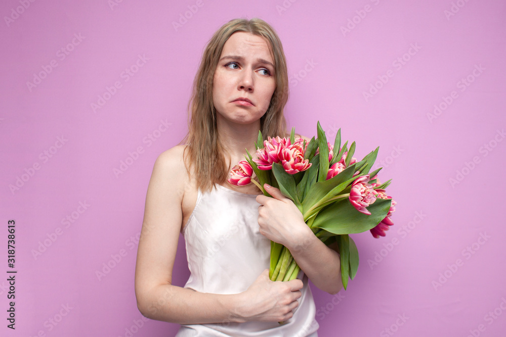 young unhappy girl with a bouquet of flowers on a pink background, a woman holds tulips and is sad