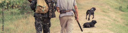 A man with a gun in his hands and an green vest on a pheasant hunt in a wooded area in cloudy weather. Hunter with dogs in search of game.