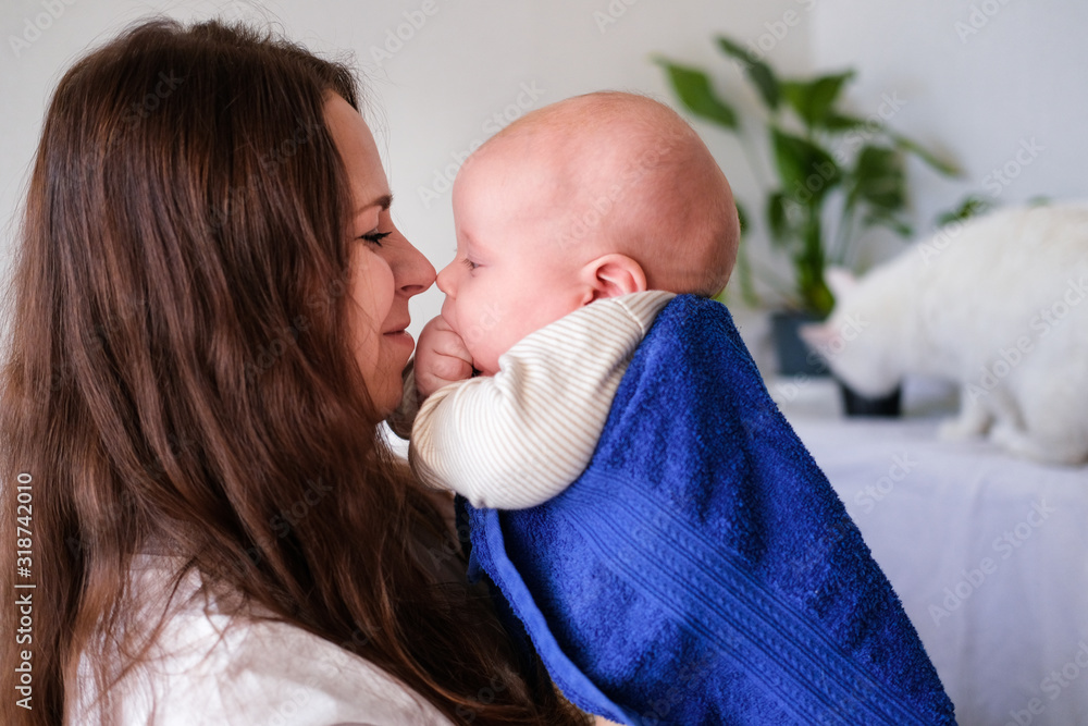 Mom hugs her little cutest baby after bath with blue towel on head