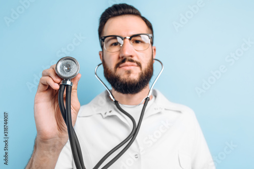 Young happy confident doctor standing with a stethoscope around his neck, on a light blue background