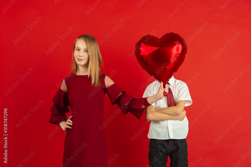 Heart-shaped balloon. Valentine's day celebration, happy, cute caucasian kids isolated on red studio background. Concept of human emotions, facial expression, love, relations, romantic holidays. Heart-shaped balloon. Valentine's day celebration, happy, cute caucasian kids isolated on red studio background. Concept of human emotions, facial expression, love, relations, romantic holidays.