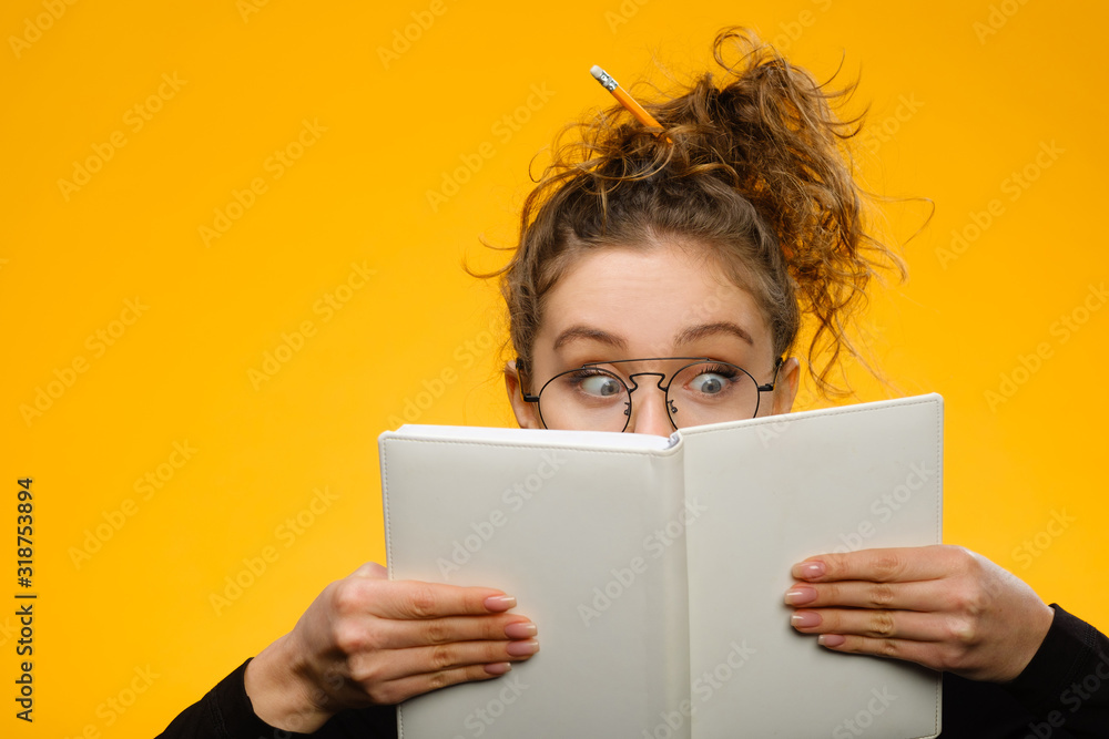 Closeup portrait of teenager hiding behind notebook Closeup portrait of teenager hiding behind notebook