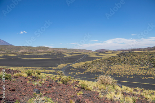 Hermoso paisaje volcánico con un camino ondulante. Predominan los colores negro, amarillo, rojizos y el cielo azul