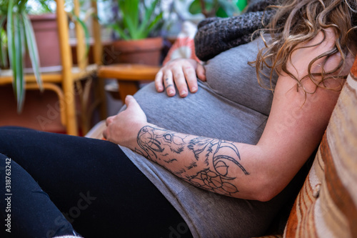 A close up shot of a heavily pregnant woman in the third trimester relaxing on sofa in family room, feeling movements and kicks with hands near labor photo