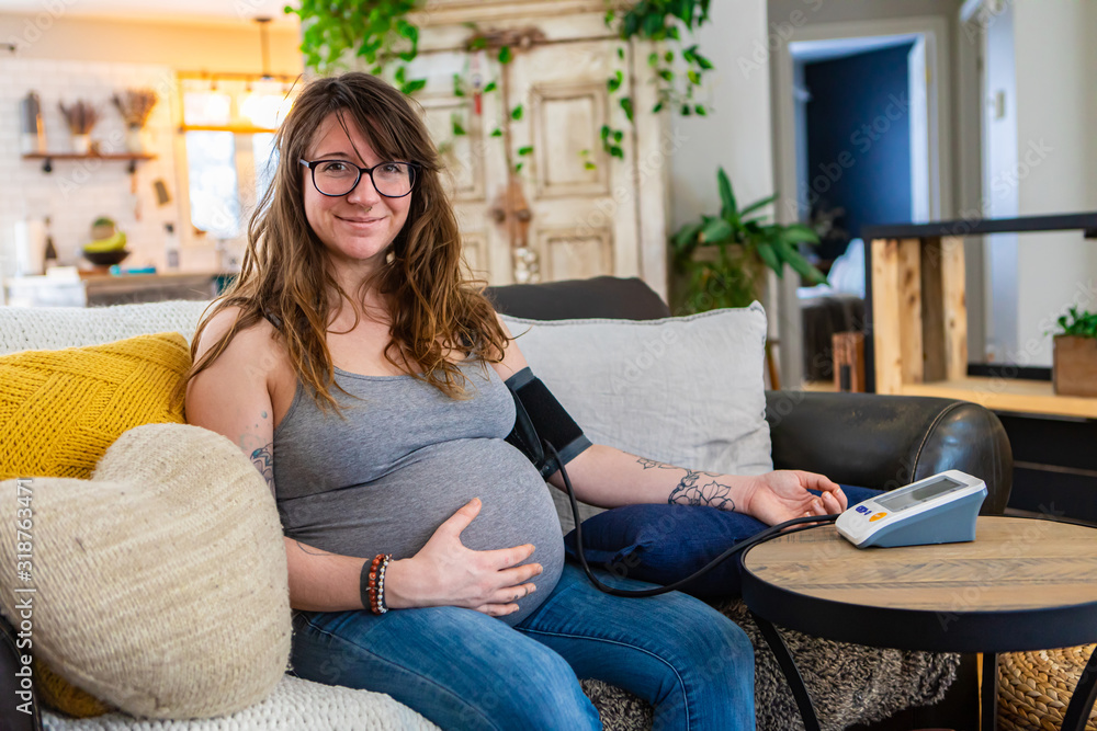 A beautiful young pregnant woman carries out prenatal health checks at home using a digital sphygmomanometer to measure blood pressure with copy space A beautiful young pregnant woman carries out prenatal health checks at home using a digital sphygmomanometer to measure blood pressure with copy space