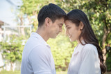 Portrait of beautiful young asian couple in casual dress touching heads with smiling and happy face in green tree background,valentine concept.