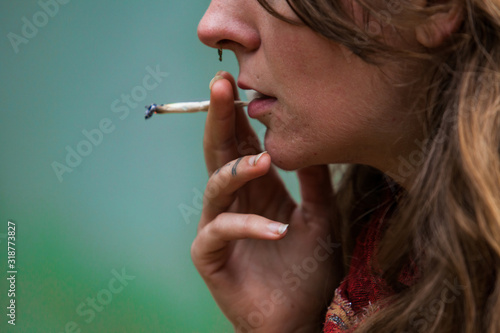 Closeup cropped shot of lower half of caucasian woman's face smoking hand rolled marijuana joint. Cannabis cigarette held by woman's tattooed fingers 