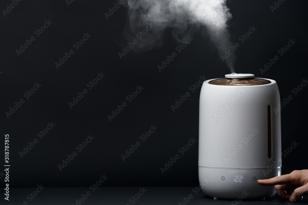 White air humidifier during work clean air and vaporizes steam up. A man's hand show the button of timer. Care about health of persons. Aromatherapy at home. Improving comfort of people.