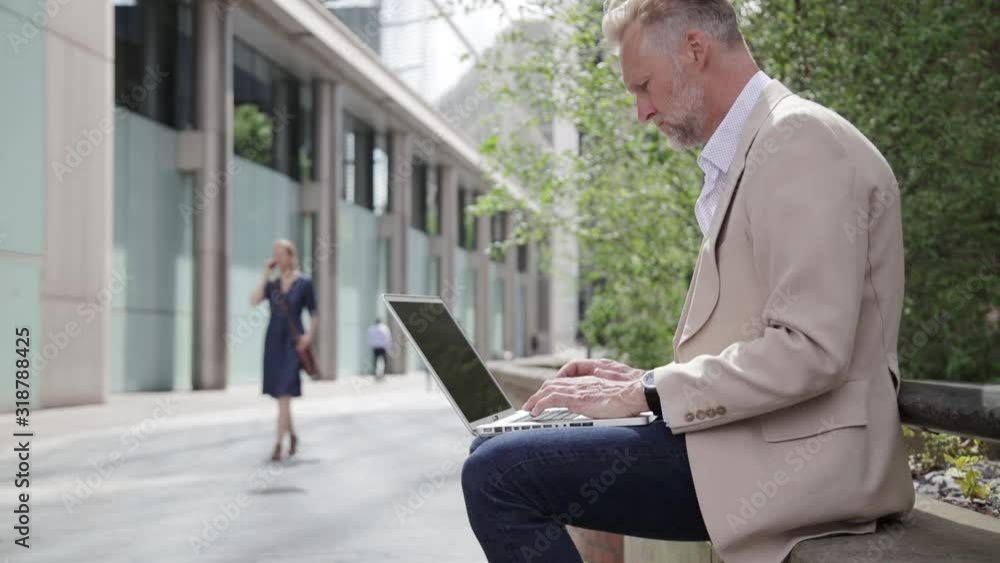Businessman working on laptop in front of office building Businessman working on laptop in front of office building