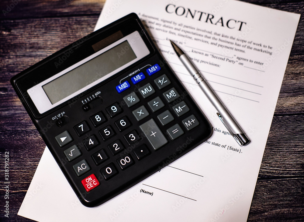 The black calculator is on the contract, next to the pen. Business concept on a wooden background. The black calculator is on the contract, next to the pen. Business concept on a wooden background.