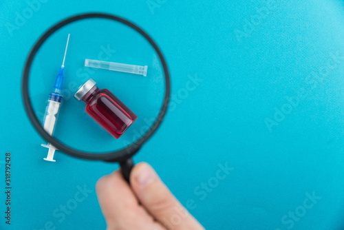 Pharmaceutical research and clinical trials concept. Medicine vial bottle for injection with vaccine and new pharmacy drug in pills and syringe under magnifying glass.