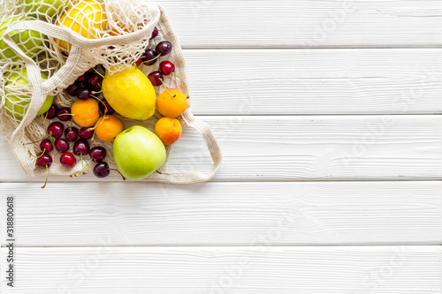 Textile eco bag with fruits on white wooden background top-down copy space