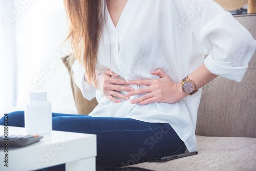 A woman having stomachache sitting on sofa and holding her belly by hands. photo