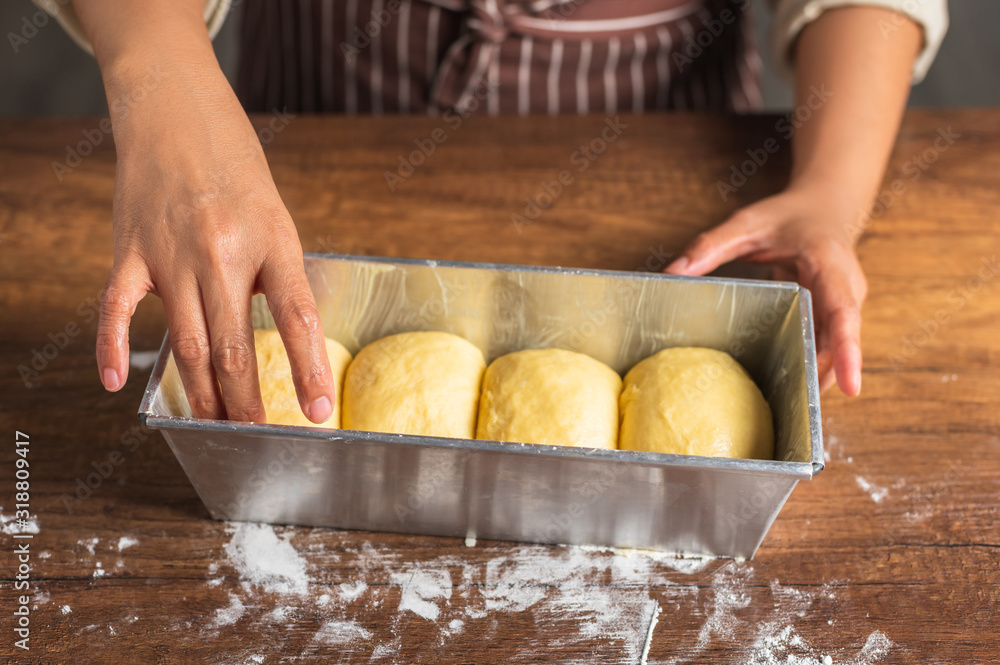 Hand stuffing brioche bread dough into a metal tin on wood texture surface table top. Hand stuffing brioche bread dough into a metal tin on wood texture surface table top.