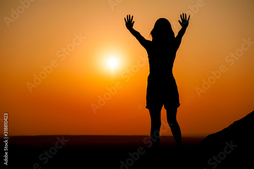 Eine Frau mit ausgestreckten Armen beim abendlichen Gebet im Gegenlicht der Sonne