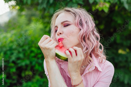 Beautiful young woman with pink hair enjoying watermelon