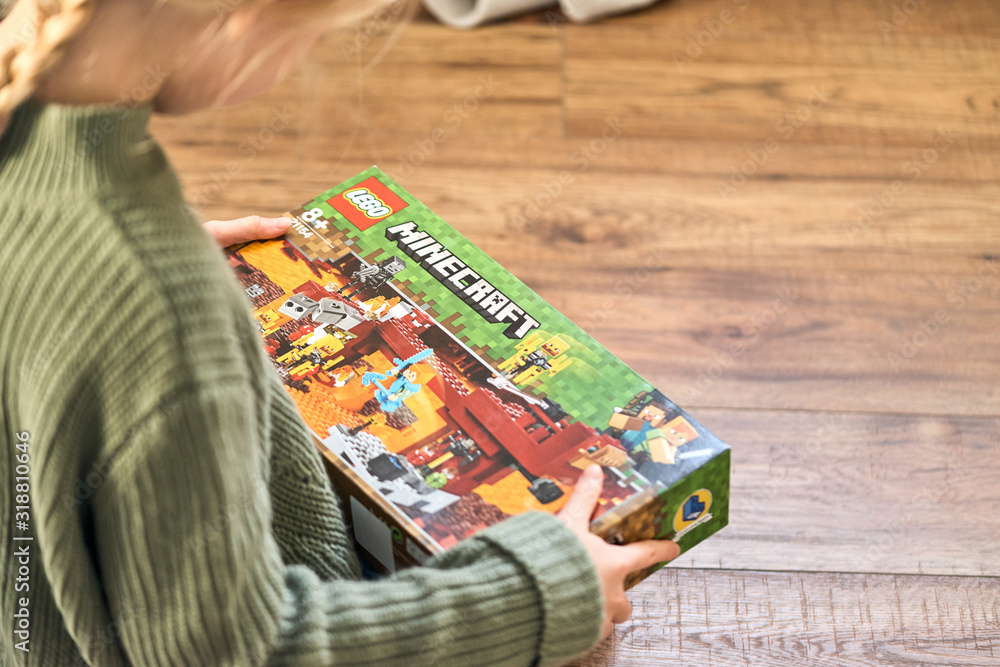 Naklejka premium January 5, 2020, Kaliningrad, Russia. A little girl with blond hair is holding a new box of Lego Minecraft and looks at it.