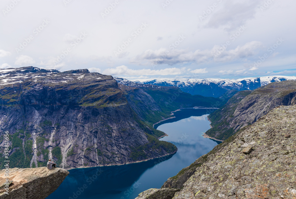 Man Sitting On Edge Of Cliff At Trolltunga Mountain In Norway.  