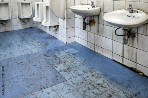 Old scruffy toilet where the floor is wet and filled with dirty footprints of student,filthy of urinals,washbasin,tiled wall, unhygienic,dirty restroom or has not cleaned the bathroom,back to school