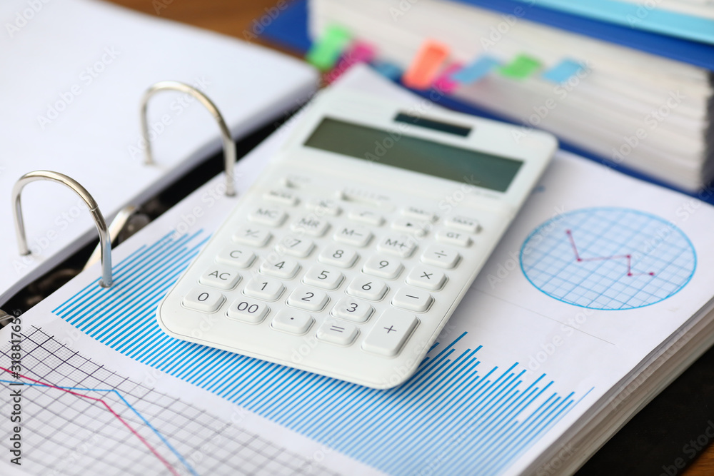 White caculator with business chart lie on the office table background closeup. Financial education concept White caculator with business chart lie on the office table background closeup. Financial education concept