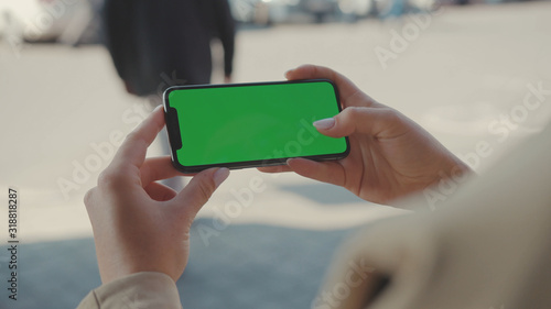 NEW YORK - May 19, 2019: Close up hands woman holding use phone horizontal green screen sitting on street scrolling pages swiping surfing internet technology smartphone message mobile phone slow