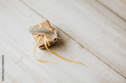 Kommunion, Konfirmation, Firmung, Taufe - Feder auf Geschenk aus Natur Papier mit gelbem Geschenkband auf weißen Holz