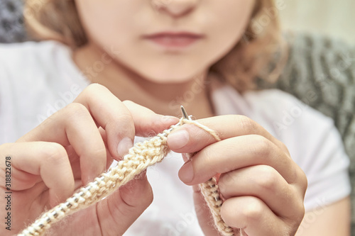A girl is knitting a beige warm sweater. A hobby of girl is knitting. Closeup