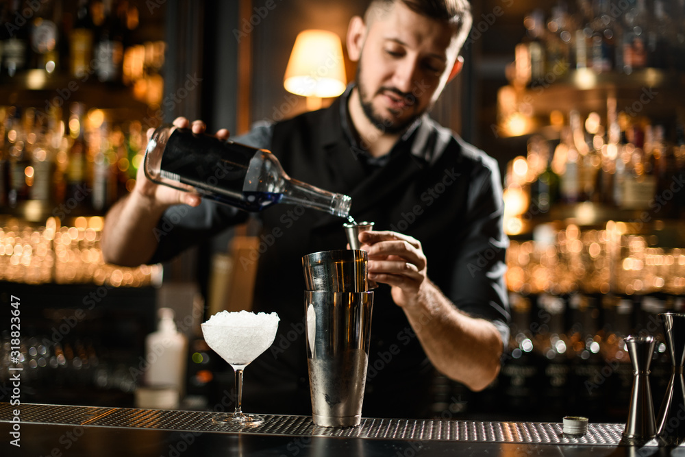 Male bartender pouring an alcoholic drink from the bottle to a steel jigger