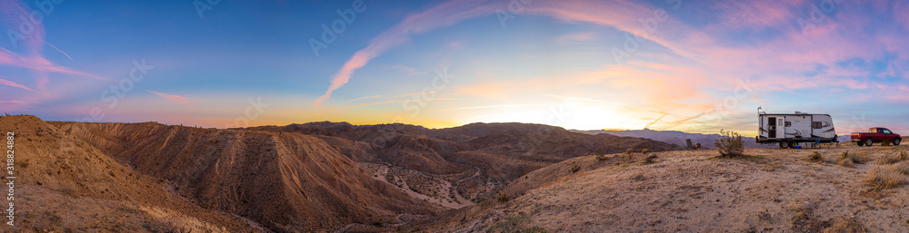 Fototapeta premium Travel trailer and pickup truck at a remote campsite on the edge of a barren canyon in Anza-Borrego Desert State Park. Some colorful sunset clouds in the sky.