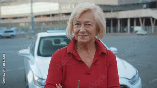 Smiling senior woman standing near car look at camera happy adventure close up handheld drive customer free time holiday journey vacation front view portrait slow motion photo